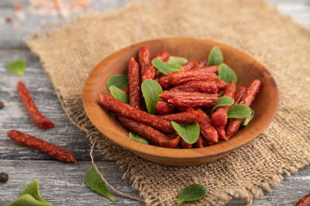 Small smoked sausage with borage microgreen, salt and pepper on gray wooden background and linen textile. Side view, close up, selective focus.の写真素材