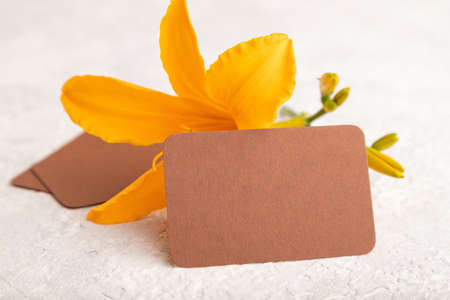 Brown paper business card mockup with orange day-lily flower on gray concrete background. Blank, side view, copy space, still life. spring concept.の写真素材