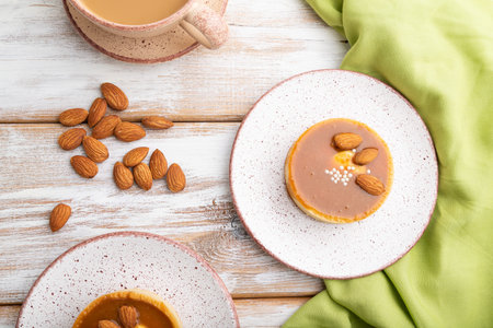 Sweet tartlets with almonds and caramel cream with cup of coffee on a white wooden background and...