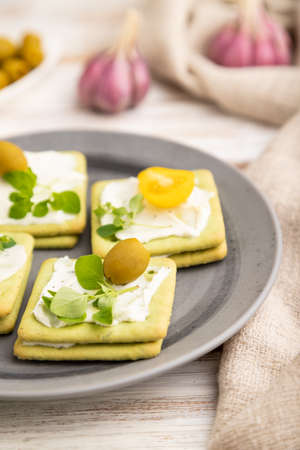 Green cracker sandwiches with cream cheese and cherry tomatoes on white wooden background and linen textile. side view, close up, selective focus.の写真素材