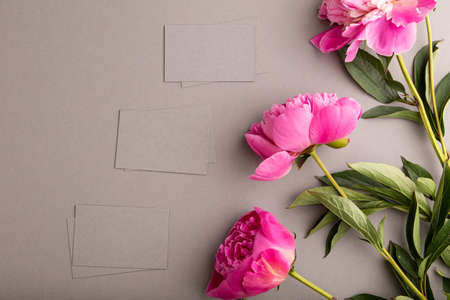 Gray business card with pink peony flowers on gray pastel background. top view, flat lay, copy space, still life. Breakfast, morning, spring concept.の写真素材