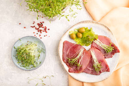 Slices of smoked salted meat with cilantro microgreen on gray concrete background and orange textile. Top view, flat lay, close up.の写真素材