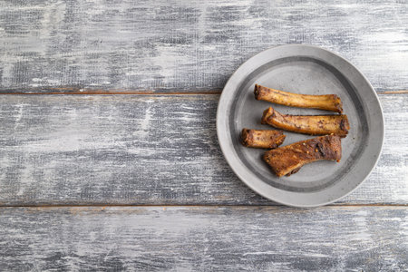 pork ribs on a wooden plate on a gray wooden background. Top view, flat lay, close up, copy space.