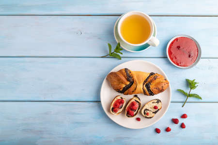Homemade sweet bun with strawberry jam and cup of green tea on a blue wooden background. top view, flat lay, copy space.の写真素材