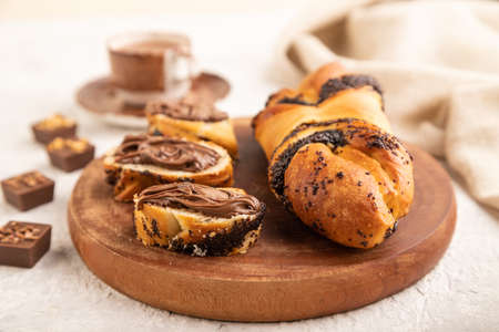 Homemade sweet bun with chocolate cream and cup of coffee on a gray concrete background and linen textile. side view, close up, selective focus.の写真素材