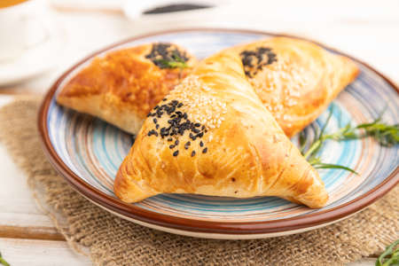 Homemade asian pastry samosa, cup of green tea on white wooden background and linen textile. side view, selective focus.の写真素材