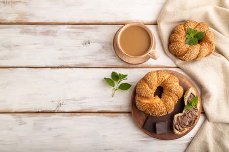 Homemade sweet bun with chocolate cream and cup of coffee on a white wooden background and linen...