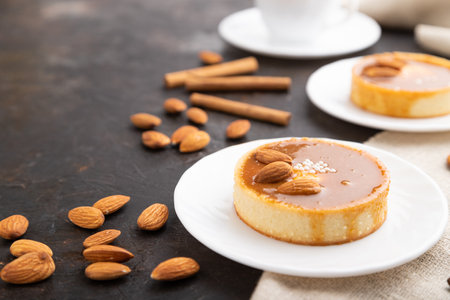 Sweet tartlets with almonds and caramel cream with cup of coffee on a black concrete background and linen textile. Side view, close up, selective focus.の写真素材