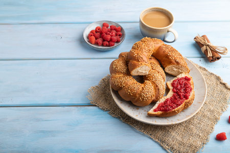 Homemade sweet bun with raspberry jam and cup of coffee on a blue wooden background and linen...