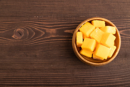 Dried and candied mango cubes in wooden bowls on brown wooden textured background. Top view, flat lay, copy space, vegan, vegetarian food concept.の写真素材