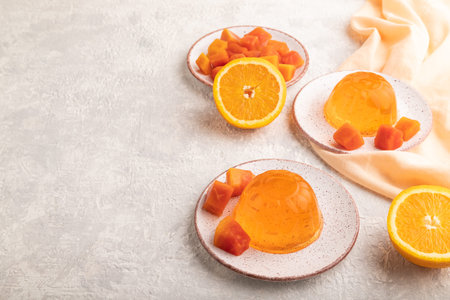 Papaya and orange jelly on gray concrete background and orange linen textile. side view, flat lay,...