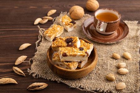 Traditional candy nougat with nuts and sesame with cup of green tea on brown wooden background and...