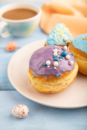 Purple and blue glazed donut and cup of coffee on blue wooden background and orange linen textile. side view, selective focus. Breakfast, morning, concept.の写真素材
