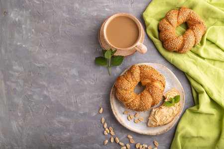 Homemade sweet bun with peanut butter and cup of coffee on a gray concrete background and green...