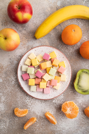 Various fruit jelly chewing candies on plate on brown concrete background. apple, banana, tangerine, top view, flat lay, close up.の写真素材