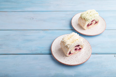 Roll biscuit cake with cream cheese and jam on blue wooden background, side view, copy space.の写真素材