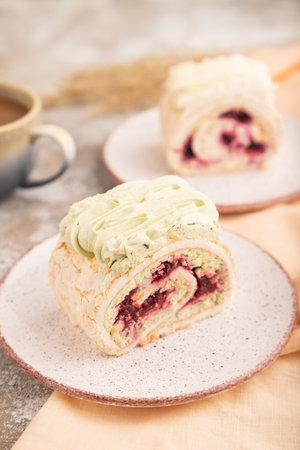 Roll biscuit cake with cream cheese and jam, cup of coffee on brown concrete background and orange linen textile. side view, close up, selective focusの写真素材