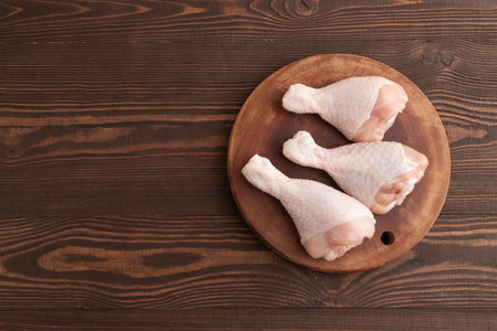 Raw chicken legs on a wooden cutting board on a brown wooden background. Top view, flat lay, copy space.の写真素材