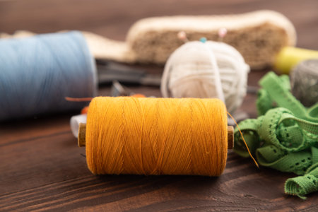 Sewing accessories: scissors, thread, thimbles, braid on brown wooden background. Side view, close...