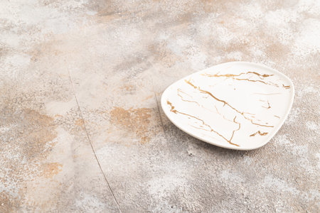 Empty white with golden pattern ceramic plate on brown concrete background. Side view, copy spaceの写真素材