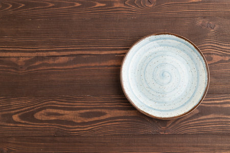 Empty blue ceramic plate on brown wooden background. Top view, copy space, flat lay.の写真素材