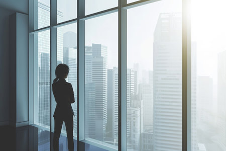 Business woman in suit in office looking at modern city with skyscrapers through panoramic window, success, wealth concept.の素材