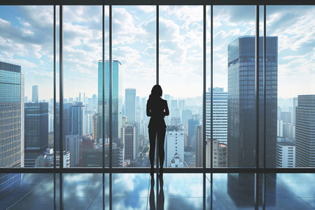 Business woman in suit in office looking at modern city with skyscrapers through panoramic window, success, wealth concept.の素材