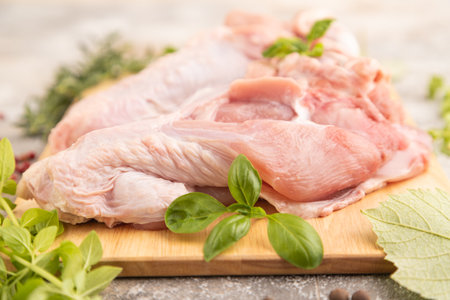 Raw turkey wing with herbs and spices on a wooden cutting board on a brown concrete background. Side view, close up, selective focus.の写真素材