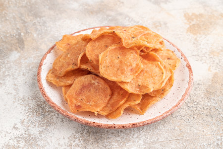 Slices of dehydrated salted meat chips with herbs and spices on gray concrete background. Side view, close upの写真素材