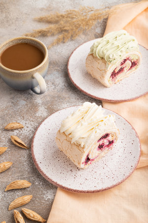 Roll biscuit cake with cream cheese and jam, cup of coffee on brown concrete background and orange linen textile. side view, close upの写真素材