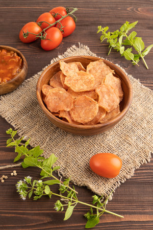 Slices of dehydrated salted meat chips with herbs and spices on brown wooden background and linen textile. Side view, close upの写真素材
