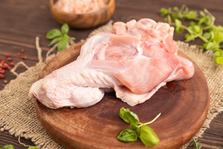 Raw turkey wing with herbs and spices on a wooden cutting board on a brown wooden background and linen textile. Side view, close up, selective focusの写真素材