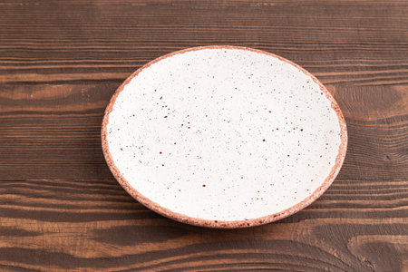 Empty white with dots ceramic plate on brown wooden background. Side view, copy spaceの写真素材