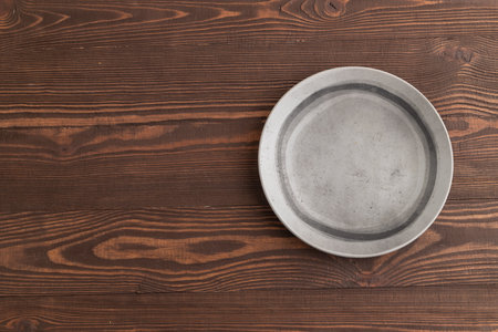 Empty gray ceramic plate on brown wooden background. Top view, copy space, flat lay.の写真素材