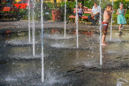 Uzhhorod, Ukraine, 30 June 2019: Children bathe in the fountain on a hot summer day. Soft focus people.のeditorial素材