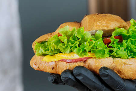 Fresh croissant with ham and lettuce in a waiter in a hand in a black gloveの写真素材