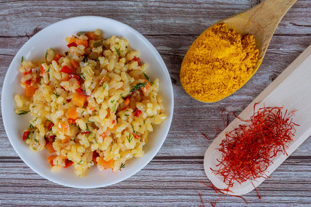 Rice with vegetables, saffron, turmeric on a white plate on a wooden background.