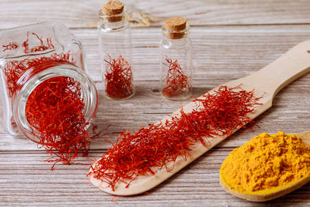 Spices on a wooden background. Saffron in a glass jar and turmeric on a wooden spoon.の写真素材