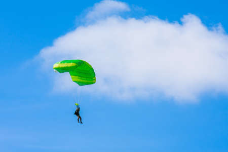 A parachutist with a light green parachute canopy against a background of blue sky and white clouds. Parachute jumping.の写真素材