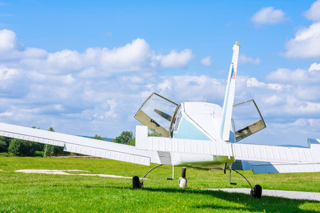 Small, 4-seater aircraft before takeoff on the field with open doors aginst blue skyの写真素材