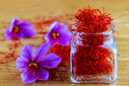 Saffron stigmas scattered on a wooden surface from a glass bottle. Saffron crocus flowers. Flowering saffron sativus.の素材 [FY310160037076]