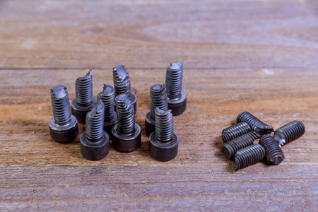 Broken black bolt on a wooden background. Hardened bolt.