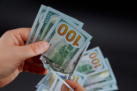 One hundred dollar bills in female hands on a black background. American money.