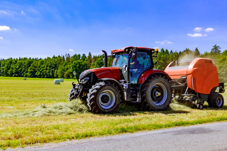 Tractor pulling a large round baler to pick up grass feed from a summer field. Blur.の写真素材