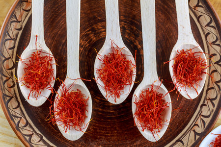 Saffron dry stamens in five wooden spoons. On a porcelain brown plate. On a wooden table.の写真素材