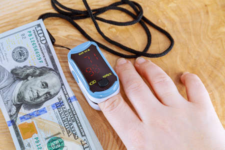 Pulse oximeter on the patient's finger. Measuring oxygen in the blood on the table. Oxygen is normal. Pay in dollars for the service.の写真素材