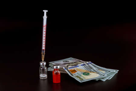 Vaccines and dollars on a black background, a set of liquid in an insulin syringe. Vaccine sale, preparation for vaccination.の写真素材