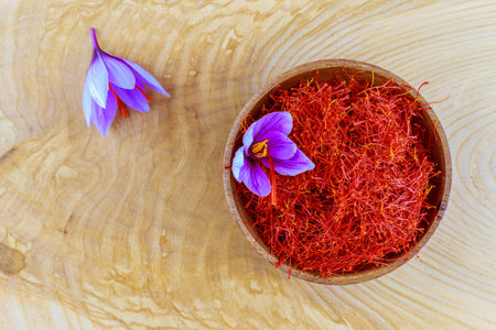 Dried saffron spices and saffron flower in a wooden plate on a wooden table. Stamens are used for cooking.