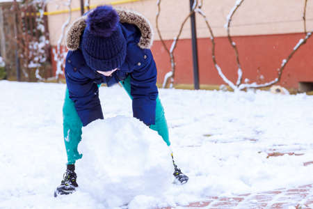 The boy is playing with snow in the yard, making a snowball. Snowy winter, children's entertainment.の写真素材
