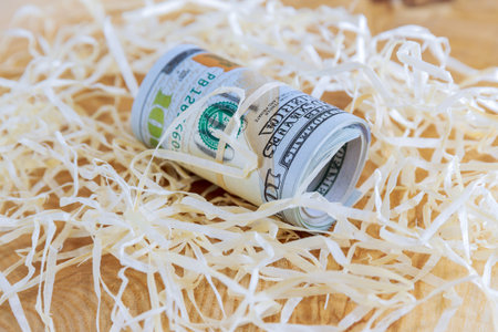 One hundred dollar bills rolled into a roll lie on a wooden decoration on the table. View from...